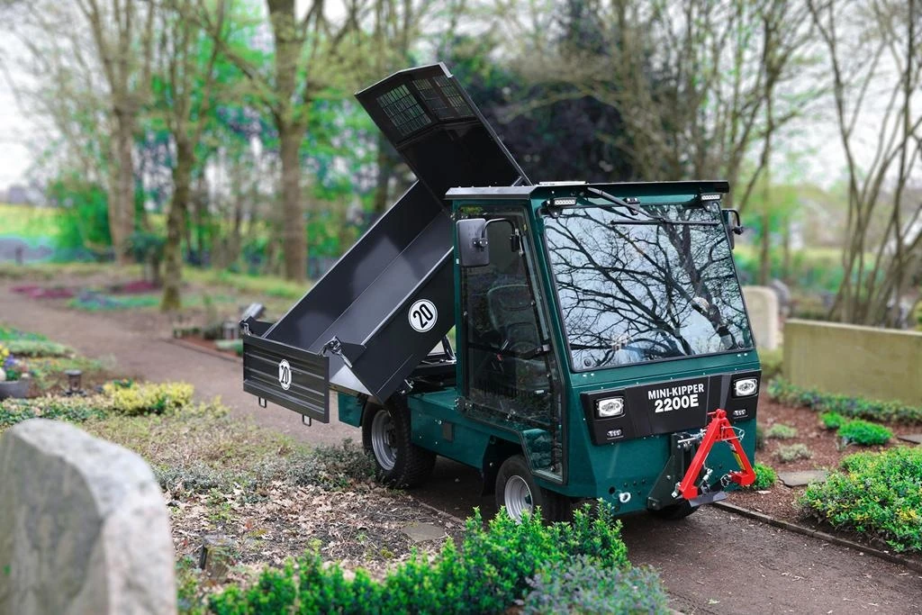 Dunkelgrüner Mini-Kipper 2200E mit hochgekippter Mulde auf einem Friedhofsweg