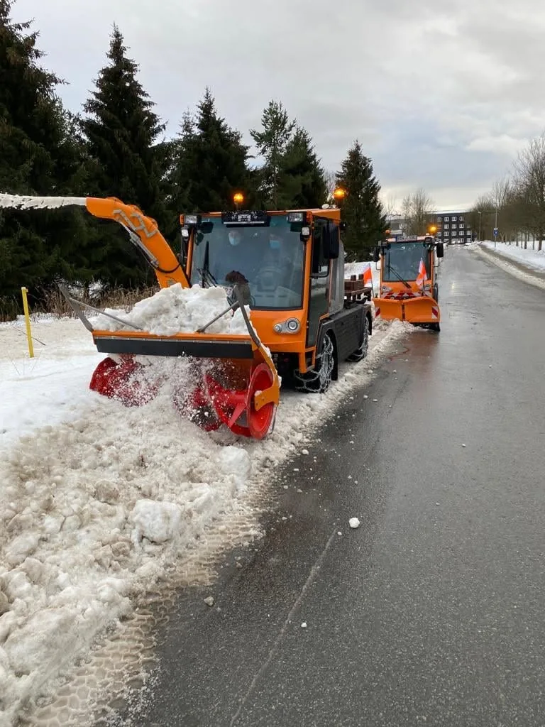 Orangefarbenes Kommunalfahrzeug mit Schneefräse im Winterdienst-Einsatz